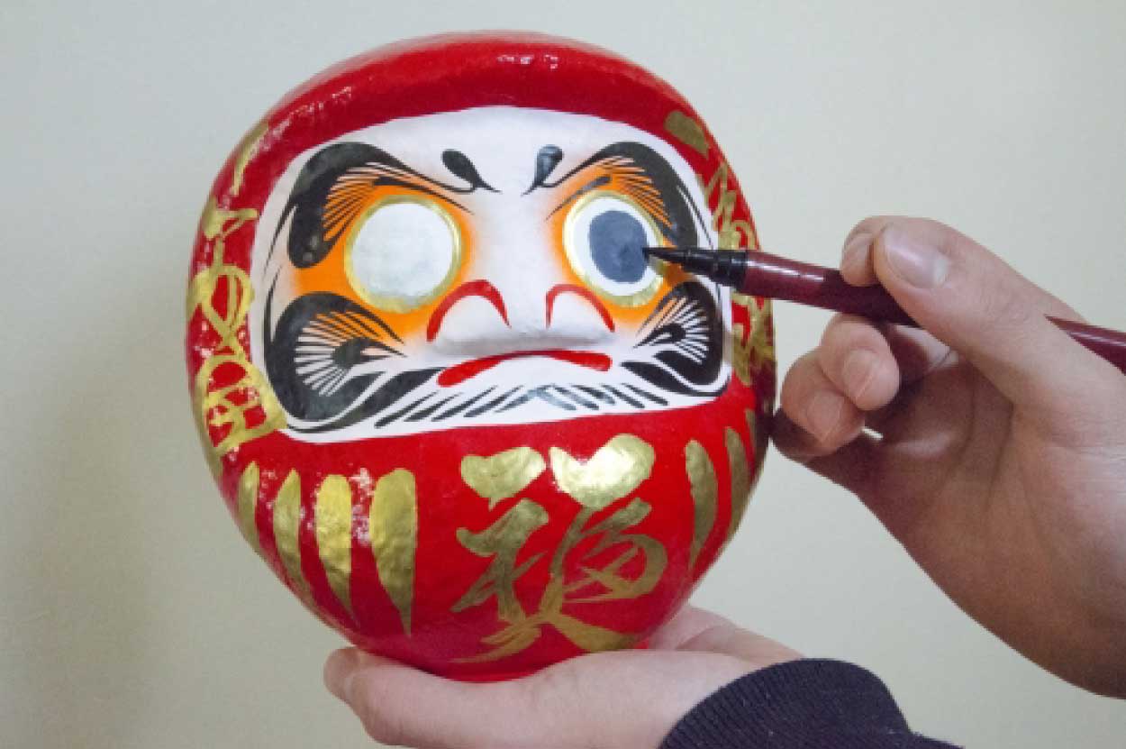筆を使ってだるまの目に黒目を入れている様子