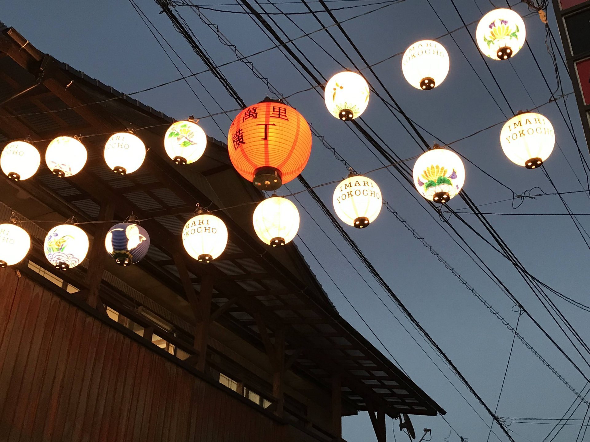 IMARI YOKOCHOの文字や花柄の提灯が夕空に並ぶ