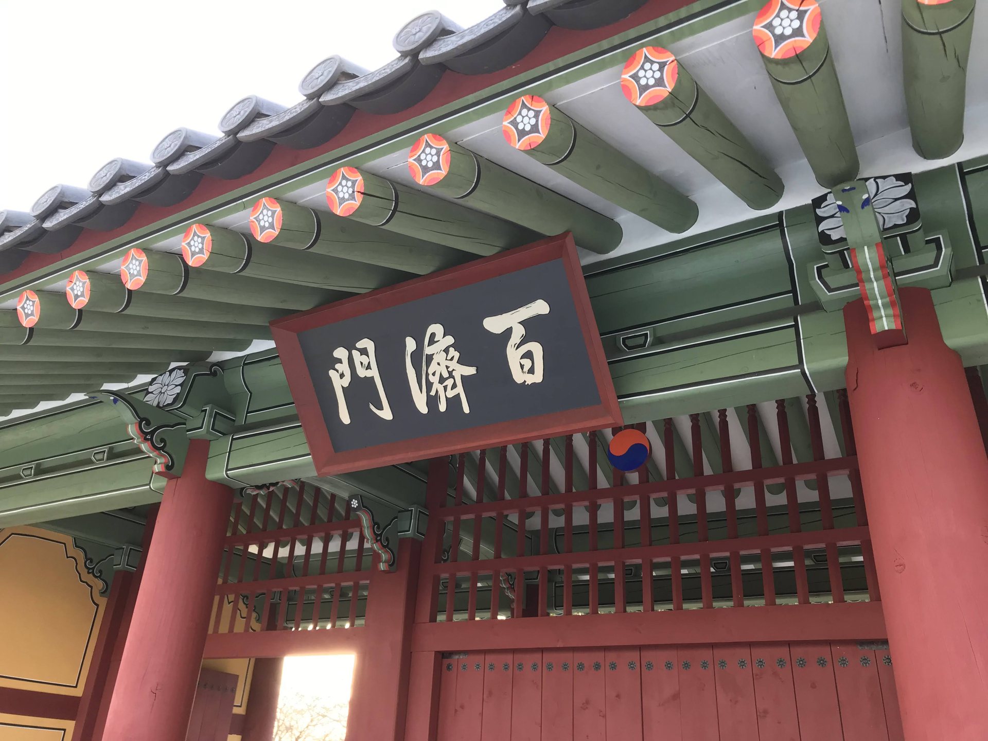 赤い柱と緑の装飾が特徴的な百済門の扁額と屋根