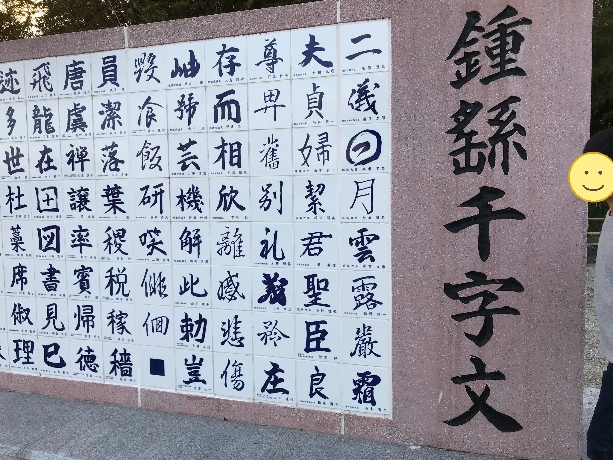 多くの漢字が並ぶ王仁博士顕彰公園の鍾繇千字文碑と見入る子ども