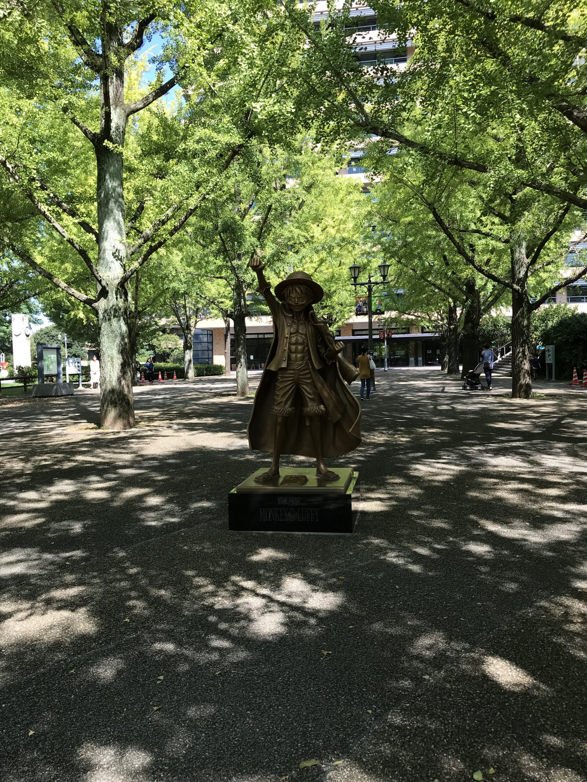 熊本県庁プロムナードの木々の下に立つルフィ像（2022年）