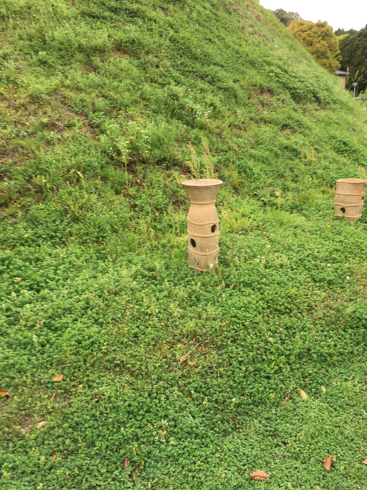 古墳の斜面のそばにある筒形の復元埴輪