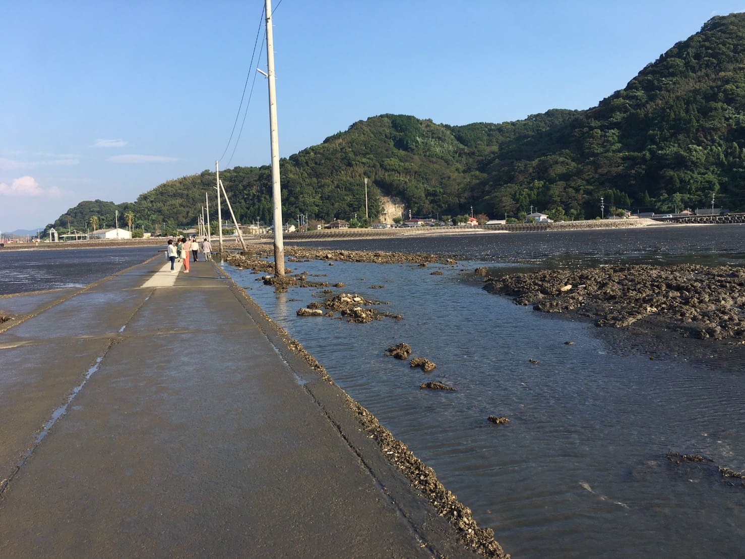 住吉海岸の長部田海床路と山並み、道の脇に残る海水（2021年）