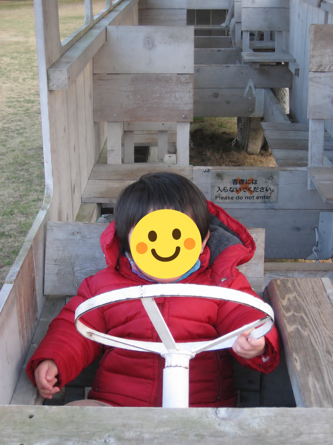 ときわ公園の木製バス型作品でハンドルを握る幼い子ども、顔はスタンプ加工済み