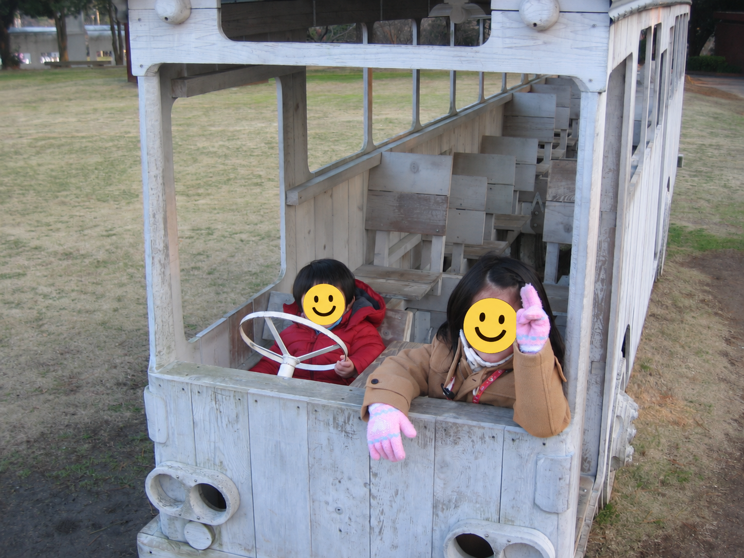 白い木製バス型作品の運転席で遊ぶ子どもたちの2014年の写真、顔はスタンプ加工済み