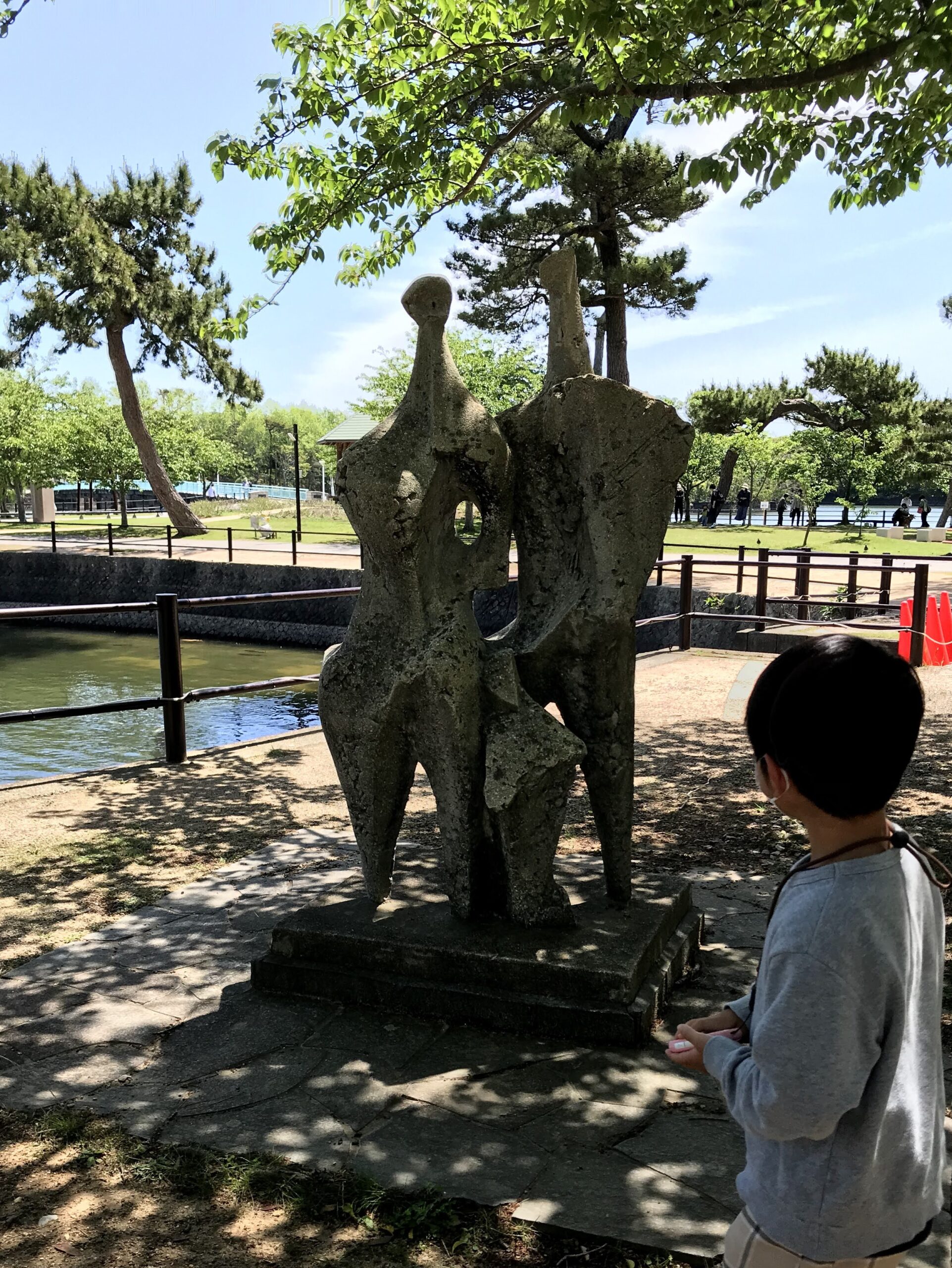 水辺の近くにある複雑な形の石の彫刻を見つめる子ども