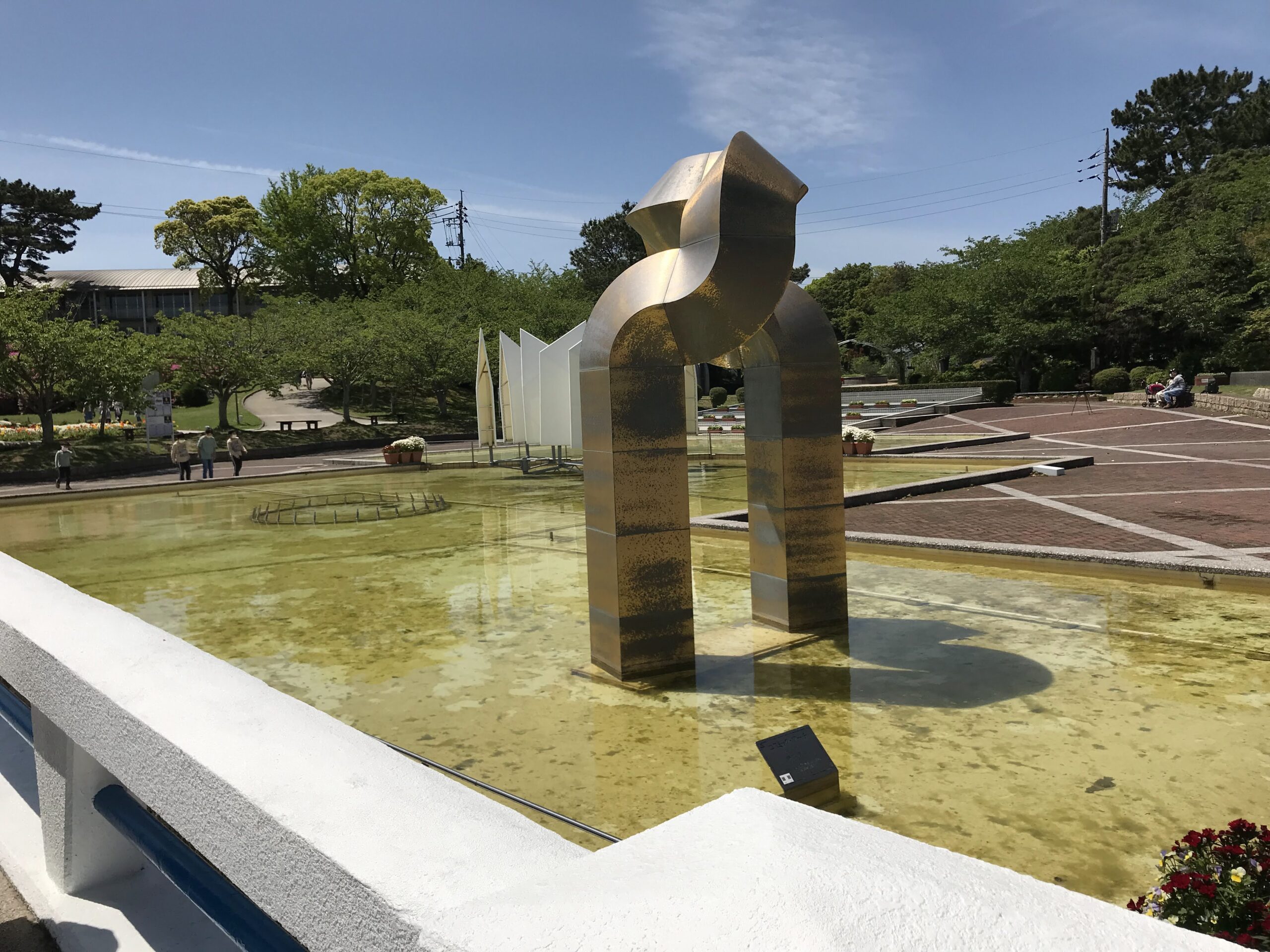 ときわ公園の浅い水面に立つ金色のアーチ状の金属彫刻
